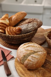 Photo of Wicker bread basket with freshly baked loaves and knife on white marble table in kitchen, closeup