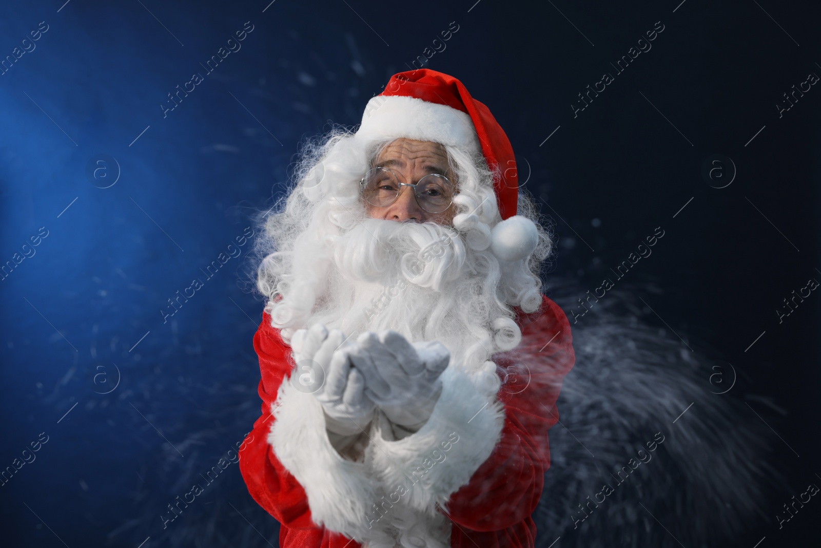 Photo of Merry Christmas. Santa Claus blowing snow on dark blue background