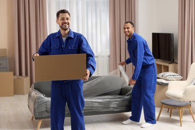 Photo of Male movers with cardboard box and sofa in new house