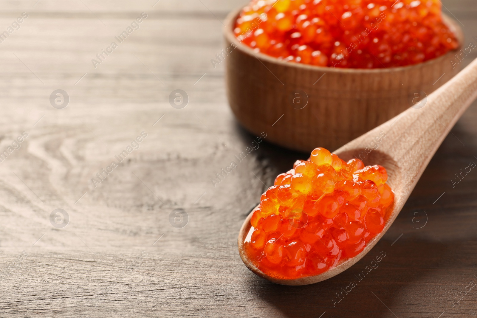 Photo of Spoon and bowl with delicious red caviar on wooden background