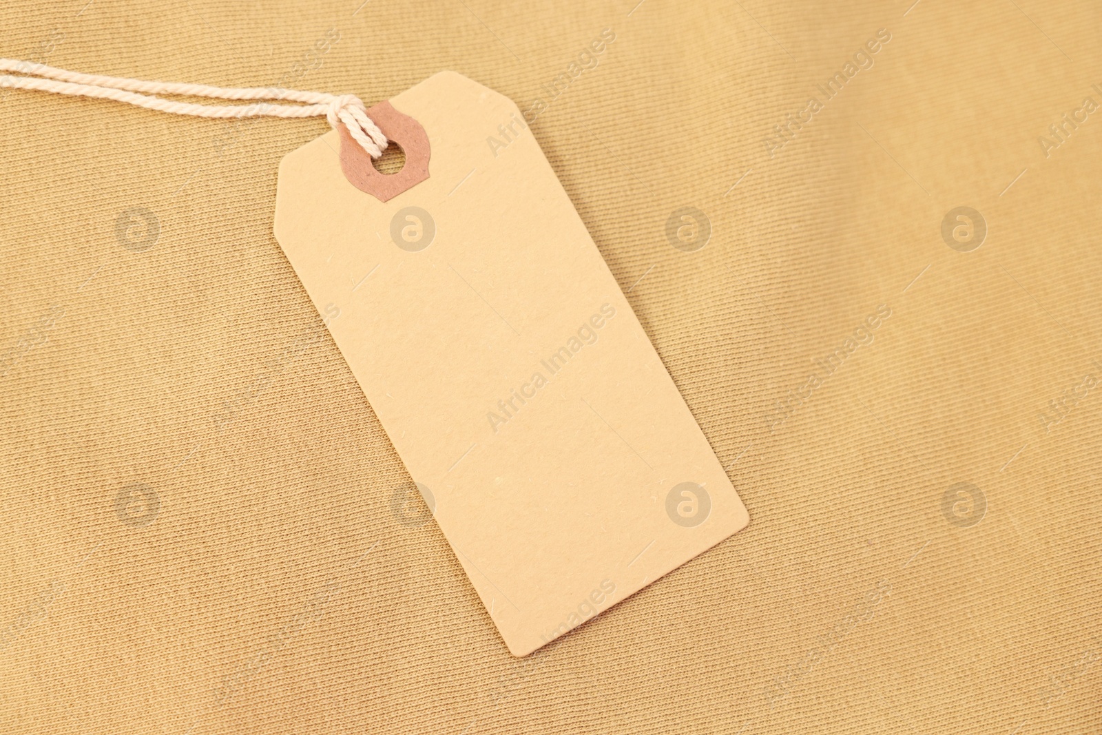 Photo of Cardboard tag on beige garment, top view. Space for text