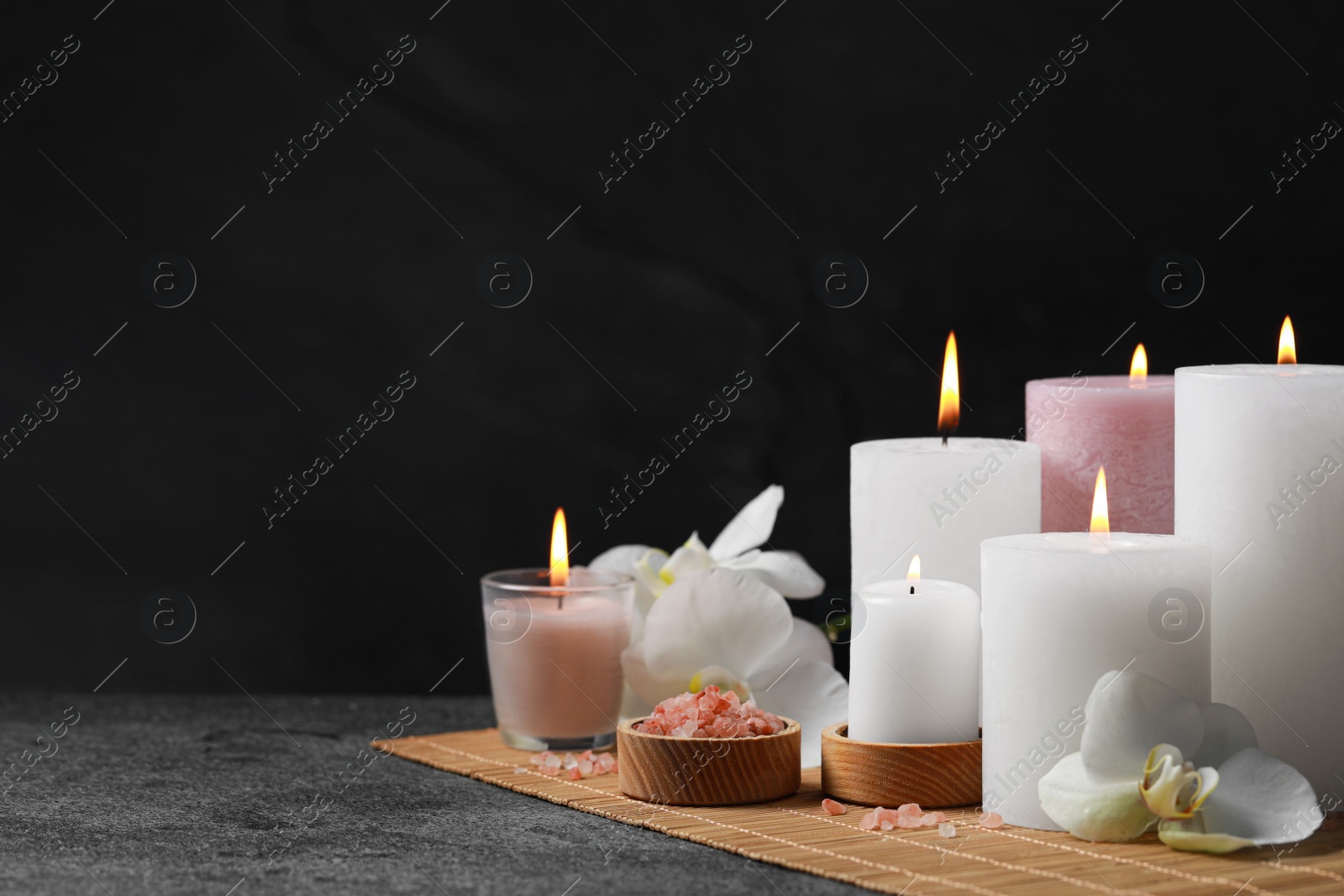 Photo of Beautiful spa composition with burning candles and flowers on dark grey table against black background. Space for text
