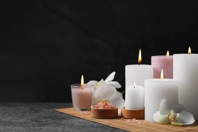 Photo of Beautiful spa composition with burning candles and flowers on dark grey table against black background. Space for text