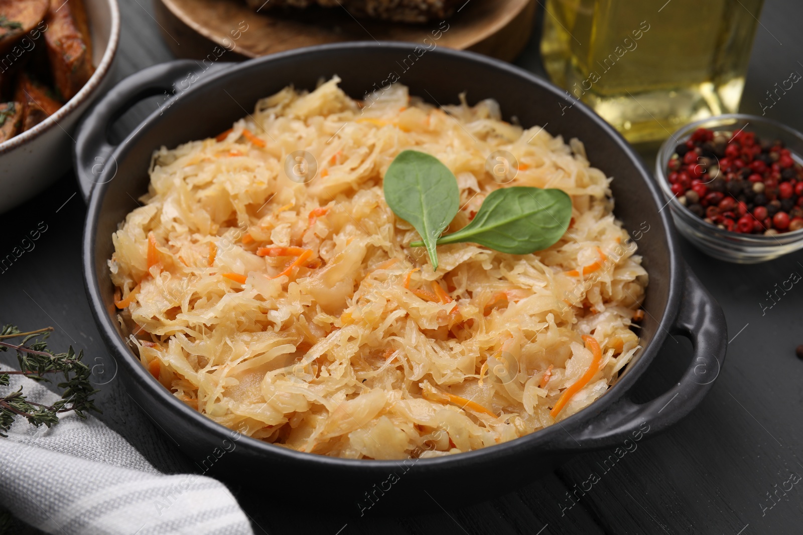 Photo of Serving pan with sauerkraut and products on black wooden table