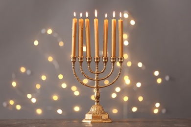 Photo of Golden menorah with burning candles on table against grey background and blurred festive lights