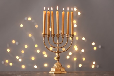 Golden menorah with burning candles on table against grey background and blurred festive lights