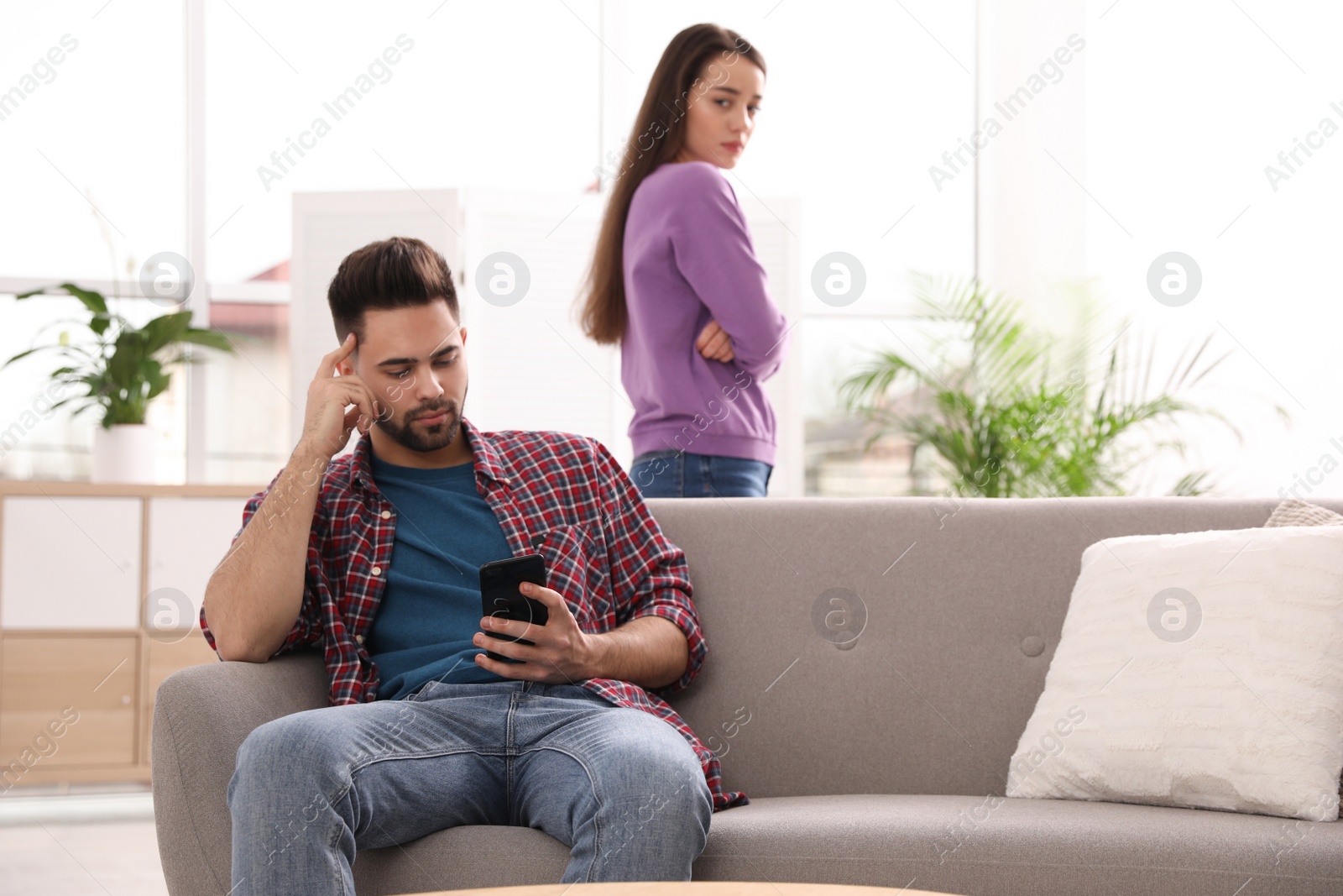 Photo of Young man preferring smartphone over his girlfriend at home