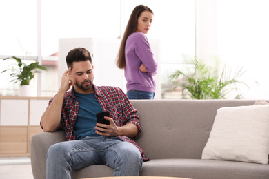 Young man preferring smartphone over his girlfriend at home
