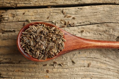 Photo of Spoon of dry dill seeds on wooden table, top view