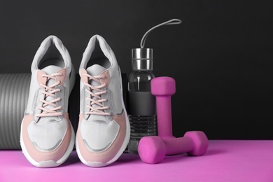 Photo of Composition of modern woman training shoes with mat, bottle and dumbbells on table. Space for text