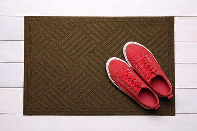 Photo of New clean door mat with shoes on white wooden floor, top view