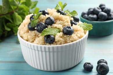 Photo of Tasty quinoa porridge with blueberries and mint in bowl on light blue wooden table, closeup