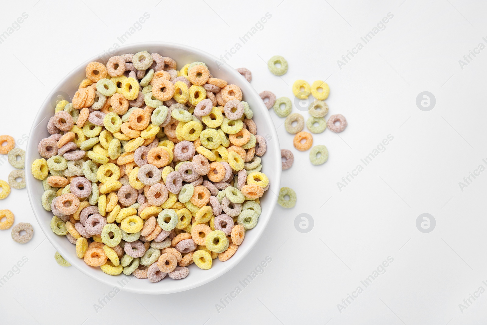 Photo of Tasty cereal rings in bowl on white table, top view. Space for text