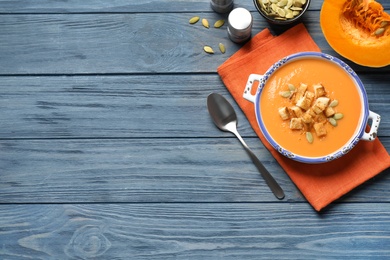 Tasty creamy pumpkin soup with croutons and seeds in bowl on blue wooden table, flat lay. Space for text
