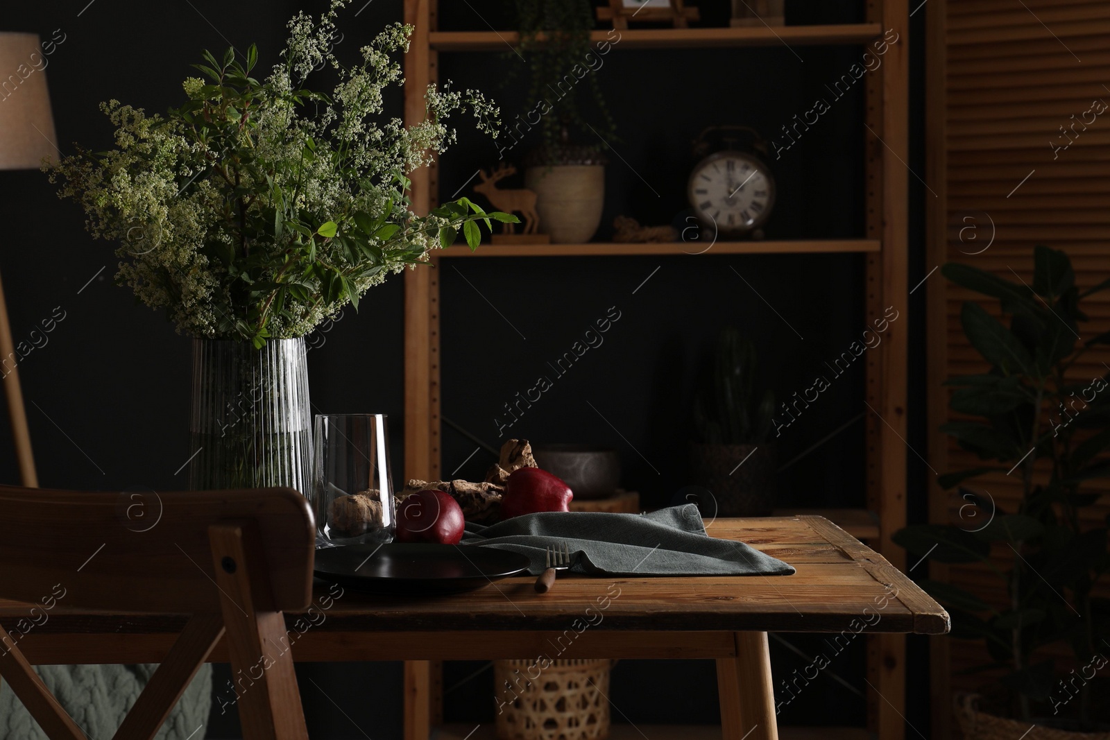 Photo of Set of clean dishware, ripe red apples and flowers on wooden table in stylish dining room