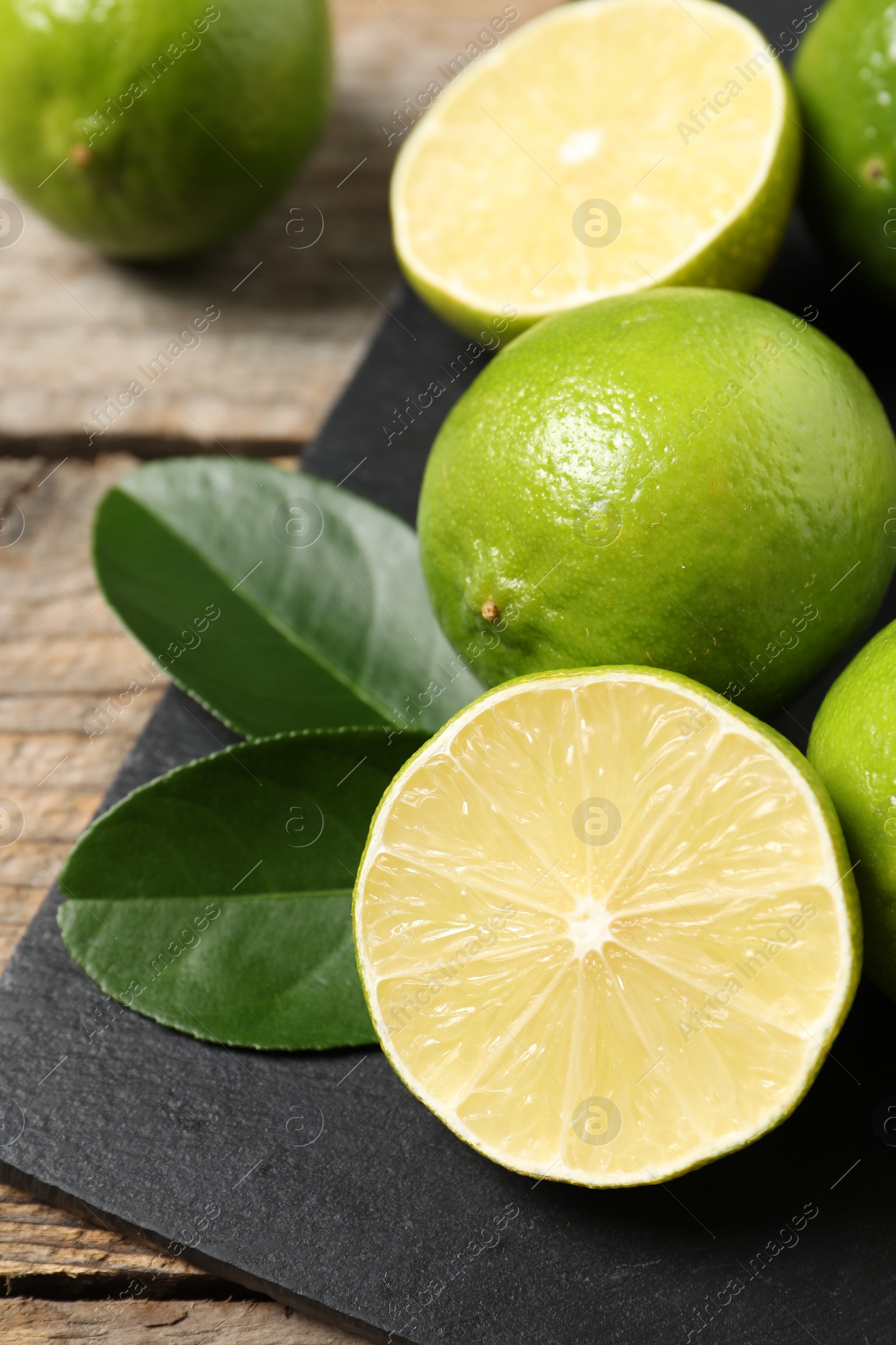 Photo of Fresh limes and green leaves on wooden table, closeup