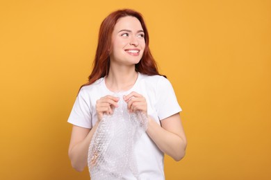 Woman popping bubble wrap on yellow background. Stress relief