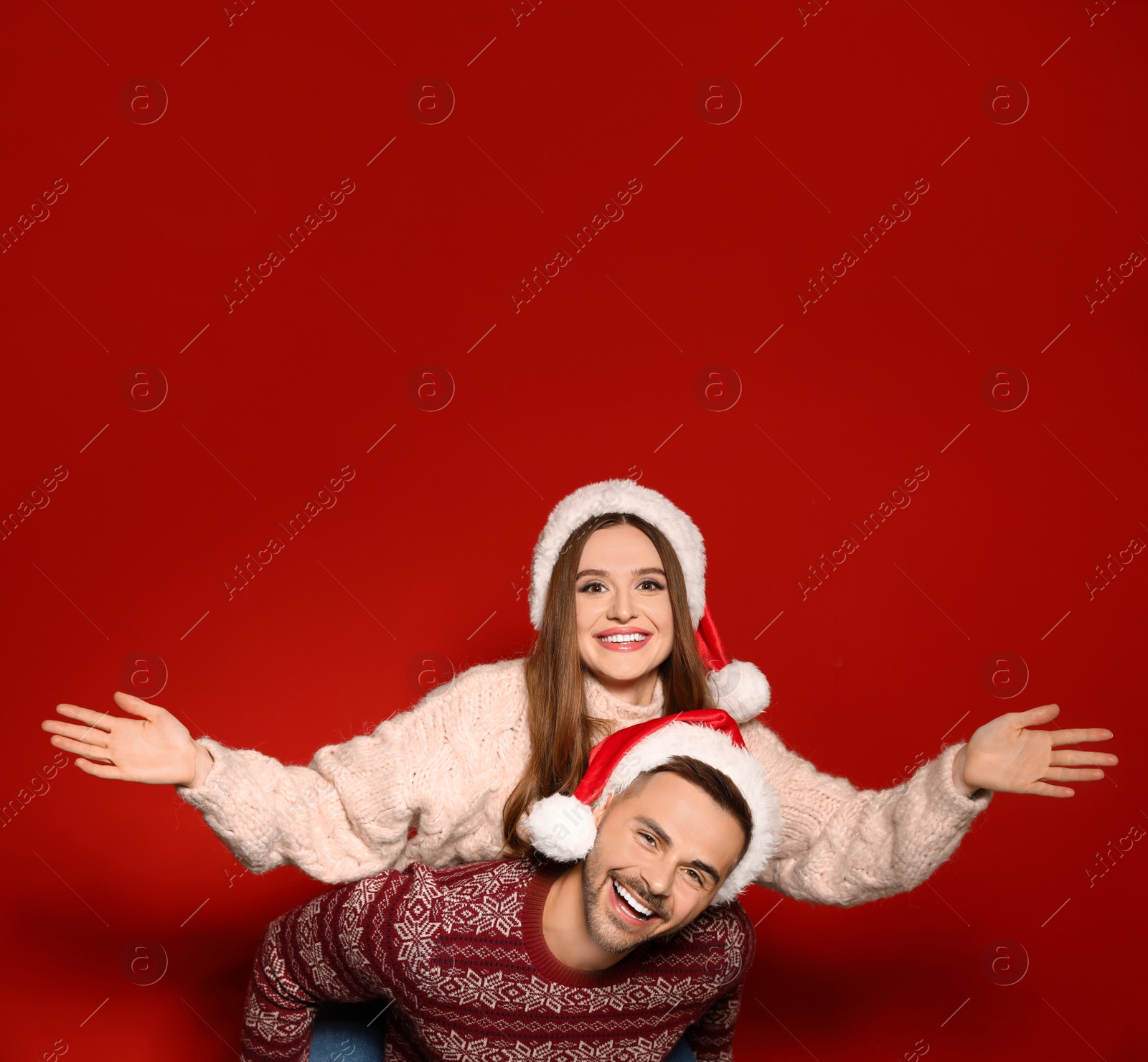 Photo of Couple wearing Christmas sweaters and Santa hats on red background