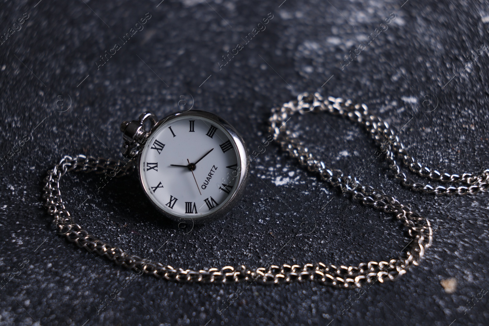 Photo of Silver pocket clock with chain on dark textured table, closeup