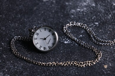 Silver pocket clock with chain on dark textured table, closeup