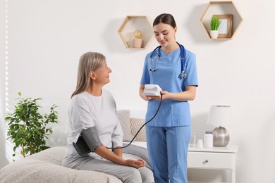 Photo of Young healthcare worker measuring senior woman's blood pressure indoors