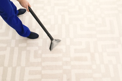 Man removing dirt from carpet with vacuum cleaner indoors, closeup. Space for text