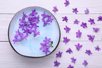 Photo of Bowl with water and flowers on white wooden table, flat lay. Spa composition