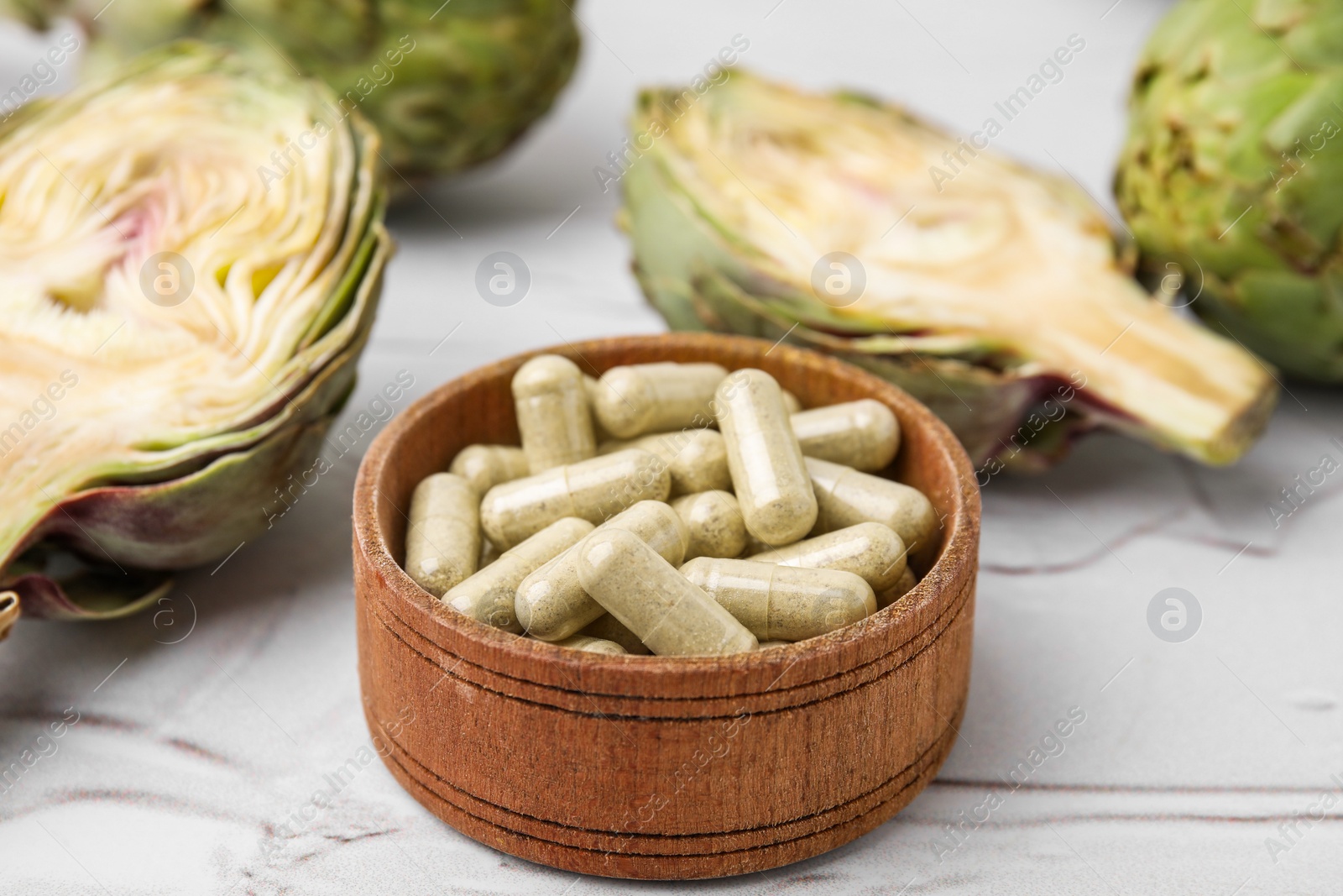 Photo of Bowl with pills and fresh artichokes on white textured table, closeup