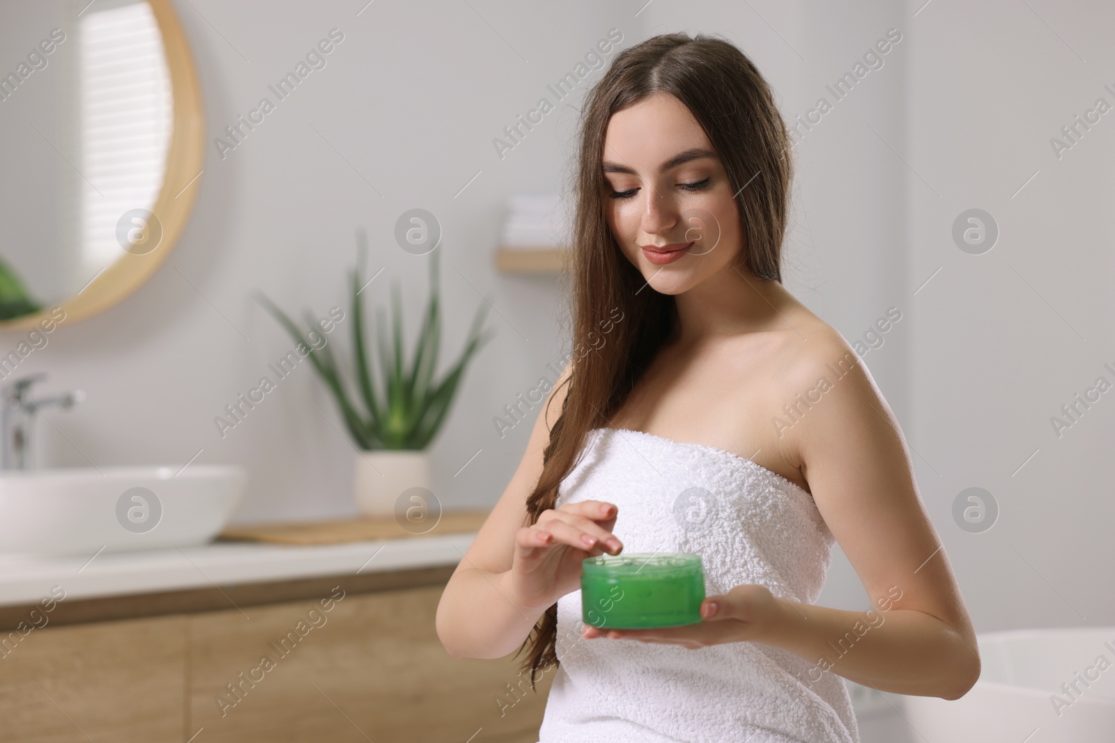 Photo of Young woman holding jar of aloe hair mask in bathroom. Space for text