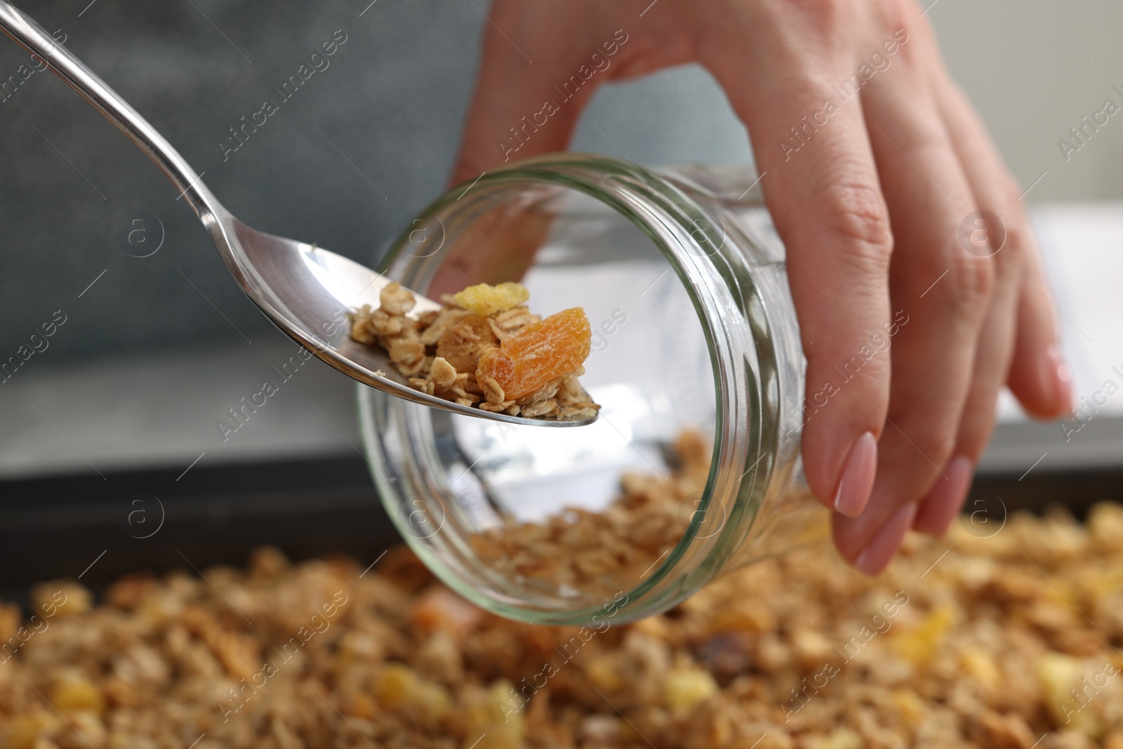 Photo of Woman putting granola into glass jar, closeup