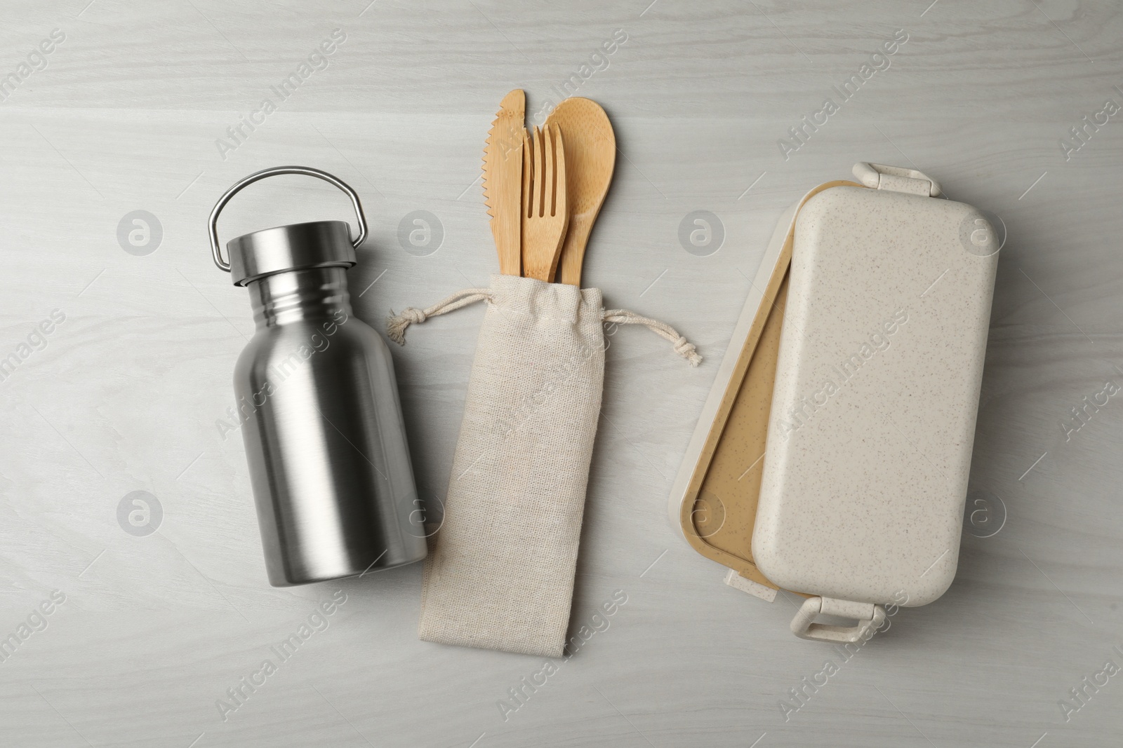 Photo of Lunch box, metal bottle and bamboo cutlery on white wooden table, flat lay. Conscious consumption