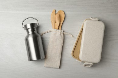 Photo of Lunch box, metal bottle and bamboo cutlery on white wooden table, flat lay. Conscious consumption