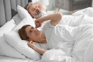 Photo of Irritated woman covering her ears in bed at home. Problem with snoring husband