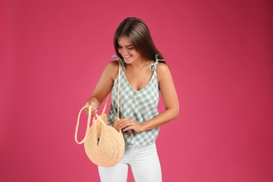 Young woman with stylish straw bag on pink background