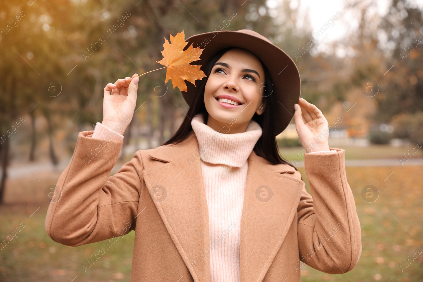 Photo of Young woman in stylish clothes holding yellow leaf outdoors. Autumn look