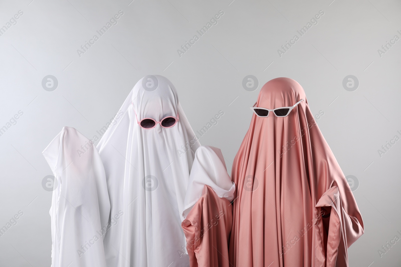 Photo of Glamorous ghosts. Women in color sheets with sunglasses on light grey background