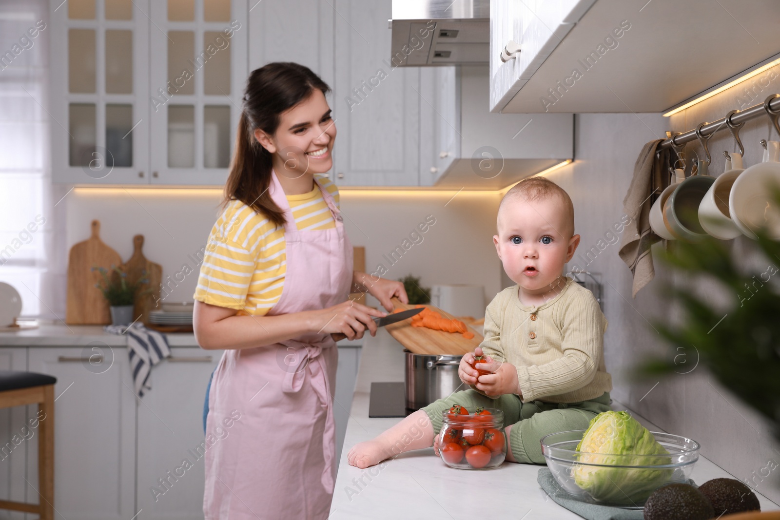 Photo of Happy young woman with her cute baby spending time together in kitchen