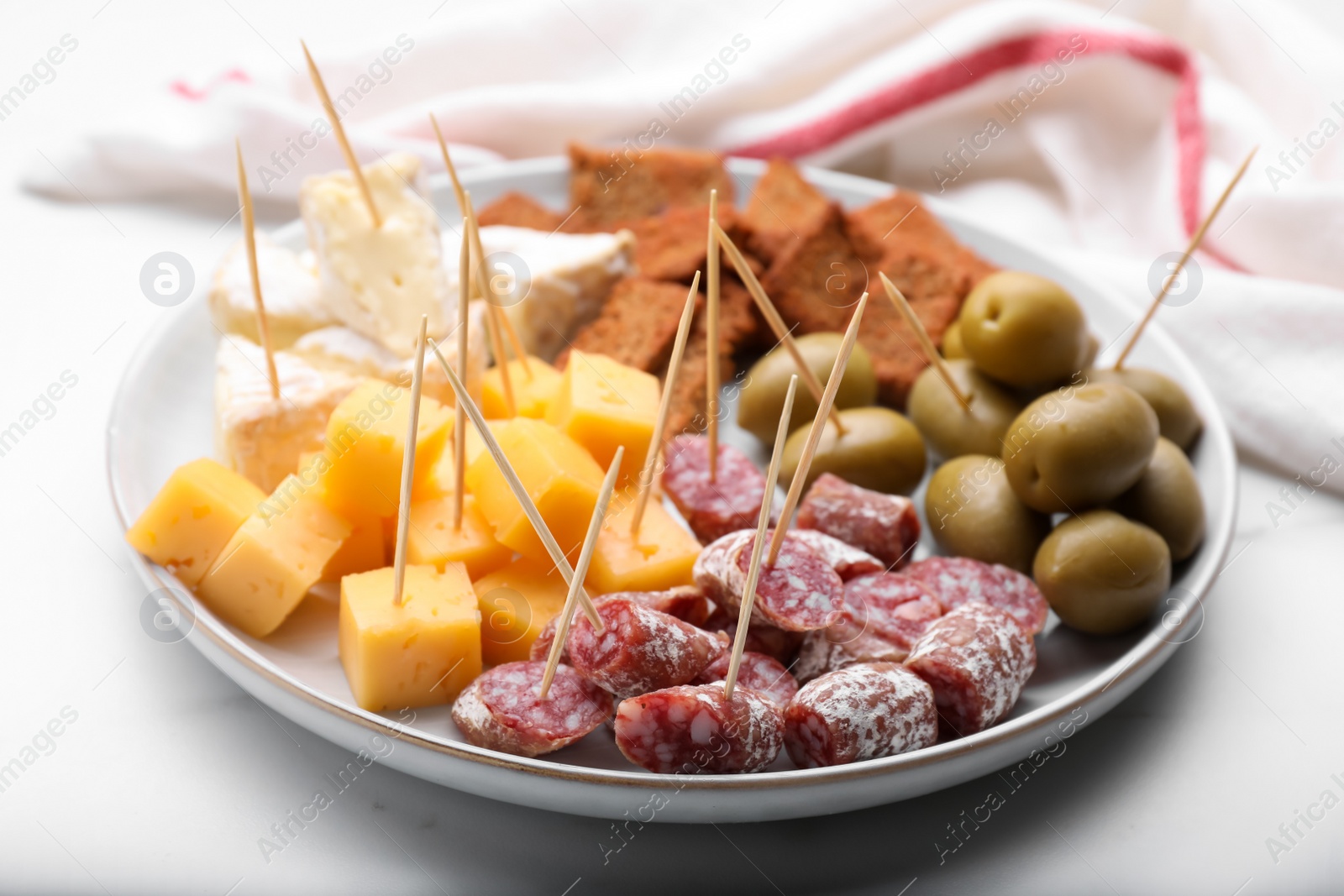 Photo of Toothpick appetizers. Pieces of sausage, cheese and olives on white table