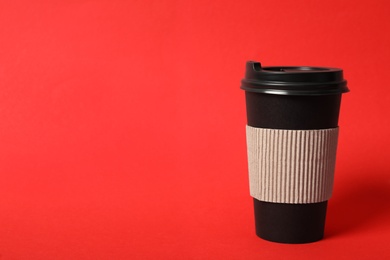 Photo of Takeaway paper coffee cup with cardboard sleeve on red background. Space for text