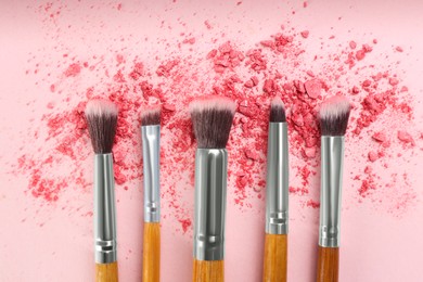 Photo of Makeup brushes and scattered eye shadow on pink background, flat lay