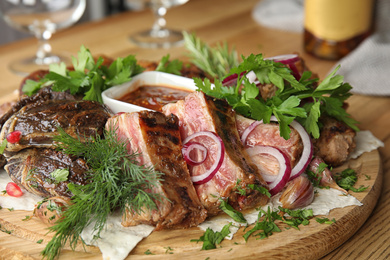 Photo of Delicious roasted ribs and liver with herbal on wooden board, closeup