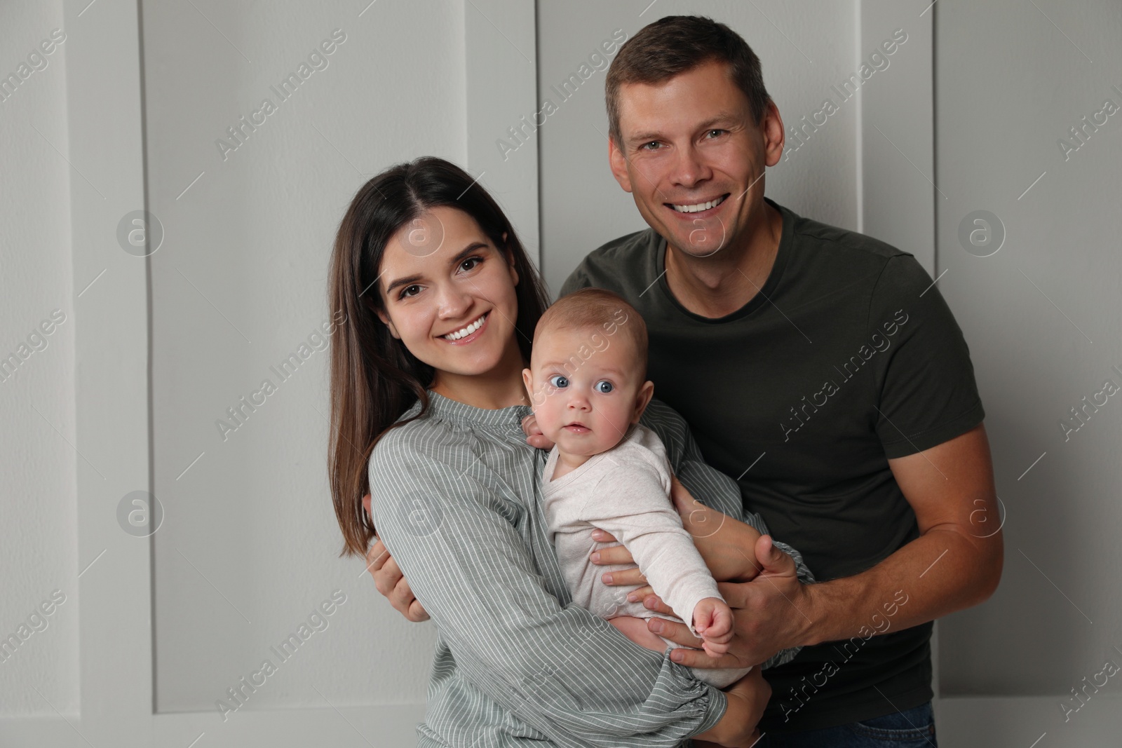 Photo of Happy family. Couple with their cute baby near light wall