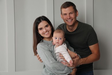 Happy family. Couple with their cute baby near light wall