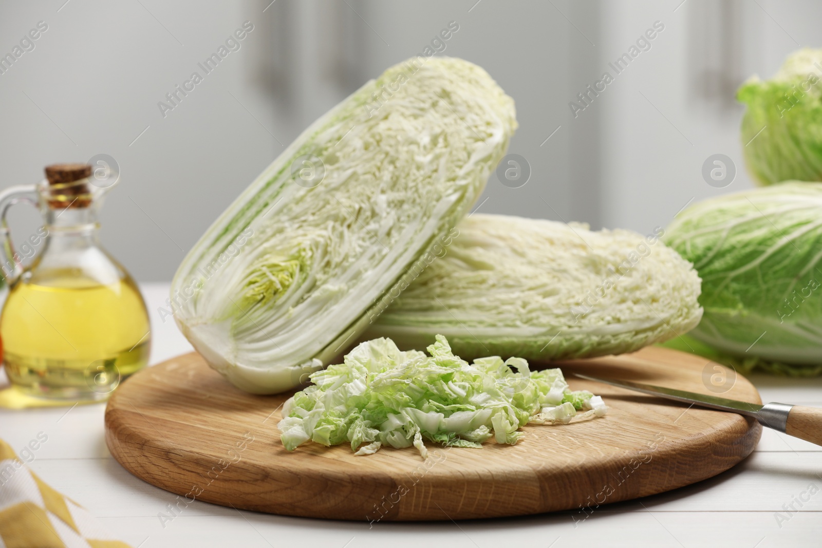 Photo of Fresh Chinese cabbages, knife and oil on white wooden table in kitchen