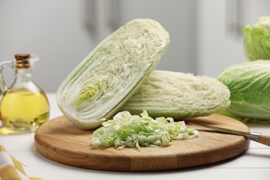 Photo of Fresh Chinese cabbages, knife and oil on white wooden table in kitchen