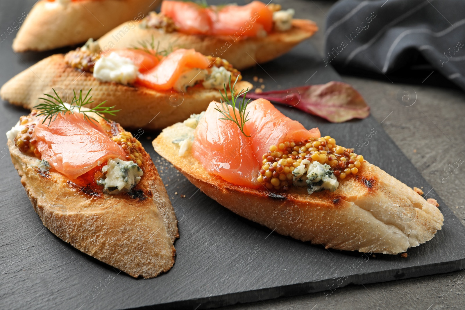 Photo of Tasty bruschettas with salmon and blue cheese on slate plate, closeup