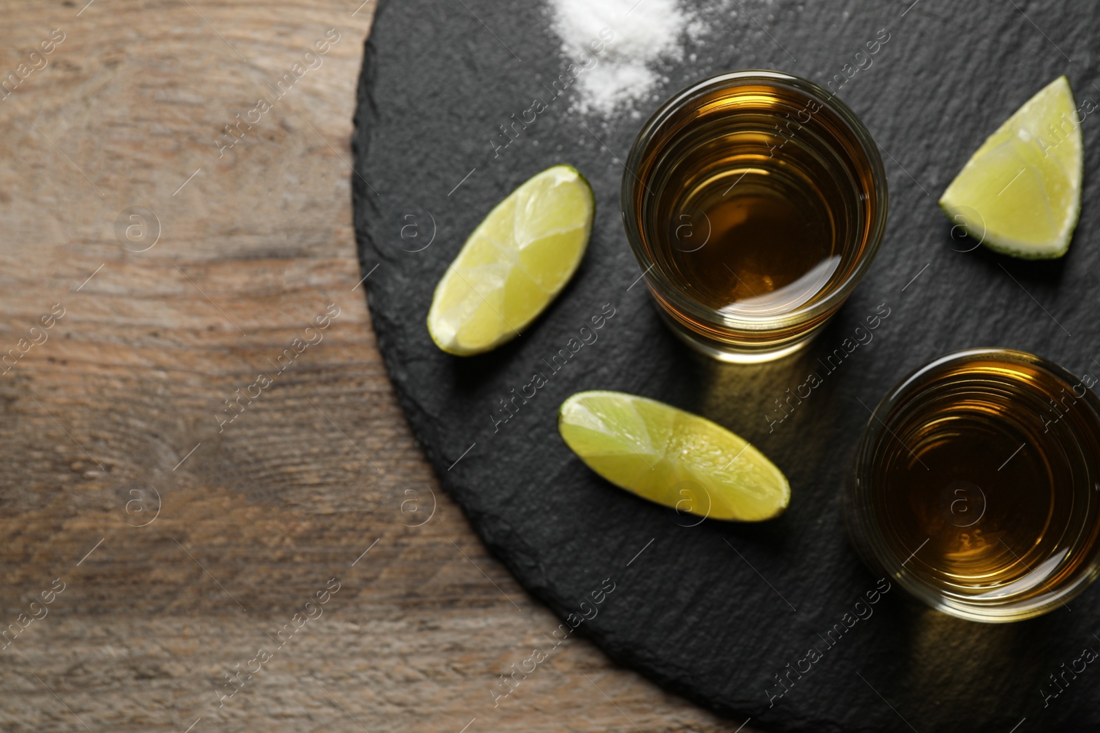 Photo of Mexican Tequila shots, lime slices and salt on wooden table, top view