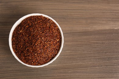 Photo of Dry rooibos leaves in bowl on wooden table, top view. Space for text
