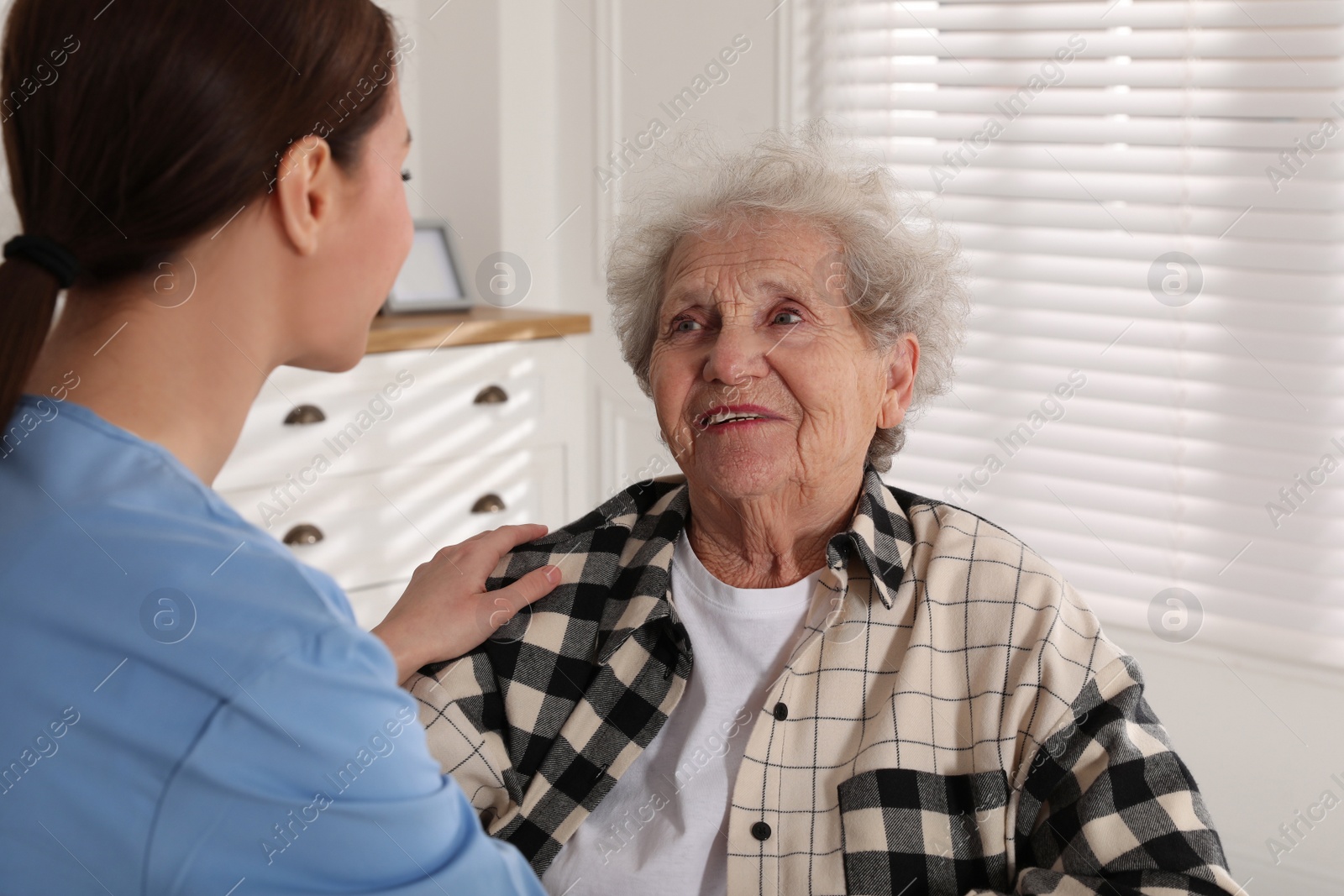 Photo of Young caregiver talking to senior woman in room. Home health care service