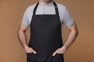 Man wearing kitchen apron on brown background, closeup. Mockup for design